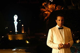 man in white suit jacket with ballerina statue behind